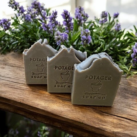 Three soaps with 'Potager Soap Co.' branding on a wooden surface with lavender in the background.