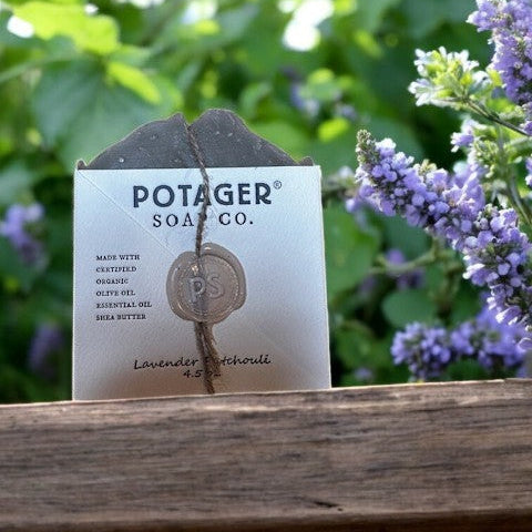 Potager Soap Co. bar of soap with a label on a wooden surface with blurred greenery and flowers in the background