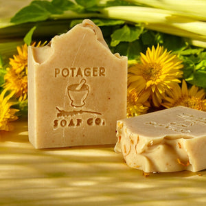 Two soap bars from Potager Soap Co. on a background of greenery and yellow flowers.