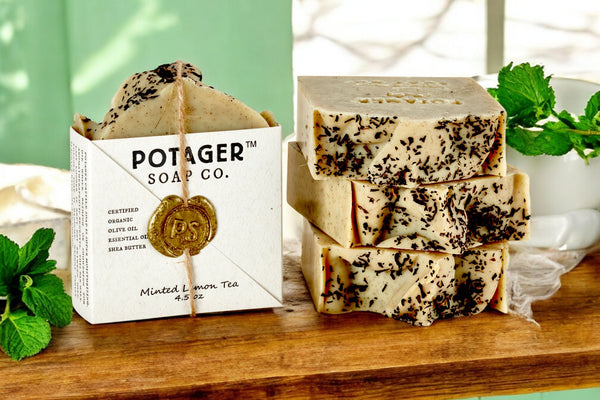 Stack of soap bars with 'Potager Soap Co.' packaging on a wooden surface.