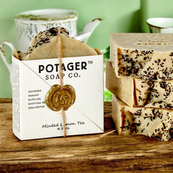 Stack of soap bars from Potager Soap Co. on a wooden surface with a green background.