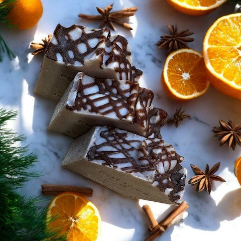 Cinnamon covered soap slices on a marble surface with oranges and star anise around.