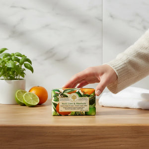 Potager Soap Co. Wavertree & London Basil Lime and Mandarin soap bar held by a hand on a wooden bathroom counter.