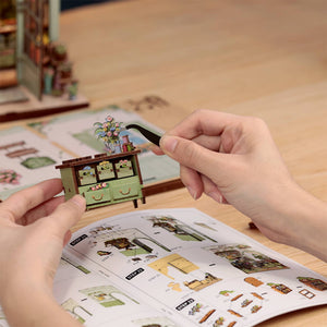 Potager Soap Co. DIY book nook kit assembly showing hands using tweezers to place a miniature floral arrangement.