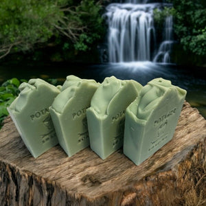 Potager Soap Co. handcrafted green eucalyptus mint bar soap arranged on a rustic tree stump with a waterfall backdrop.