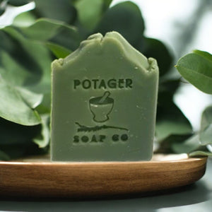 Potager Soap Co. handcrafted green eucalyptus mint bar soap on a wooden plate surrounded by fresh leaves