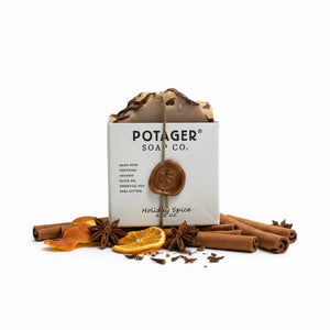 Potager Soap Co. Holiday Spice organic bar soap wrapped in paper with a wax seal, surrounded by cinnamon and orange.