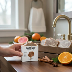 Potager Soap Co. Holiday Spice organic bar soap in white packaging with wax seal, held near a rustic wooden soap tray.