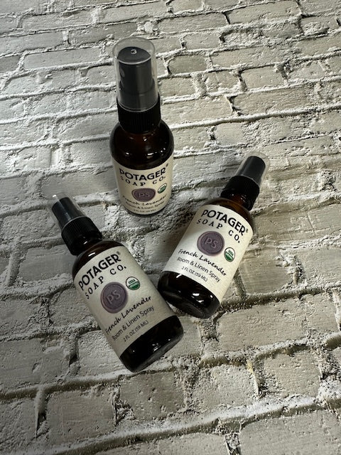 Three Potager Soap Co. French Lavender room and linen spray bottles in amber glass on a white brick background.