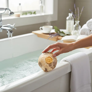 Potager Soap Co. botanical bath bomb wrapped in artisanal paper with a gold wax seal held over a steaming bathtub.