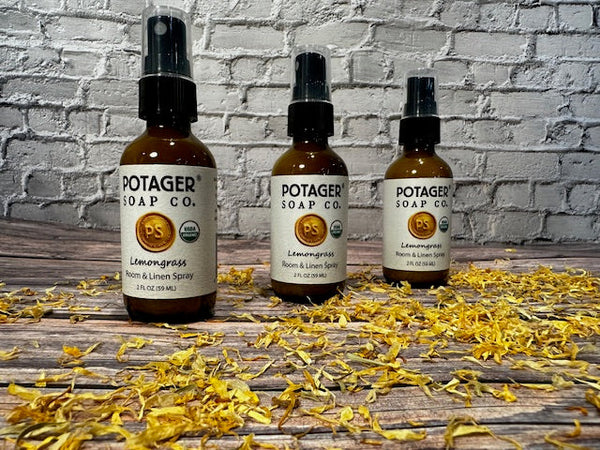 Three Potager Soap Co. amber glass bottles of organic lemongrass room and linen spray on a rustic wooden surface.