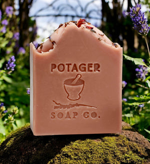 Potager Soap Co. Secret Garden organic castile soap bar with dried flower petals on a mossy stone in a garden