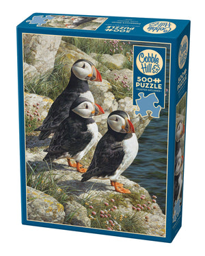 Potager Soap Co. 500-piece Cobble Hill jigsaw puzzle box featuring three Atlantic puffins on a rocky coastal cliff.