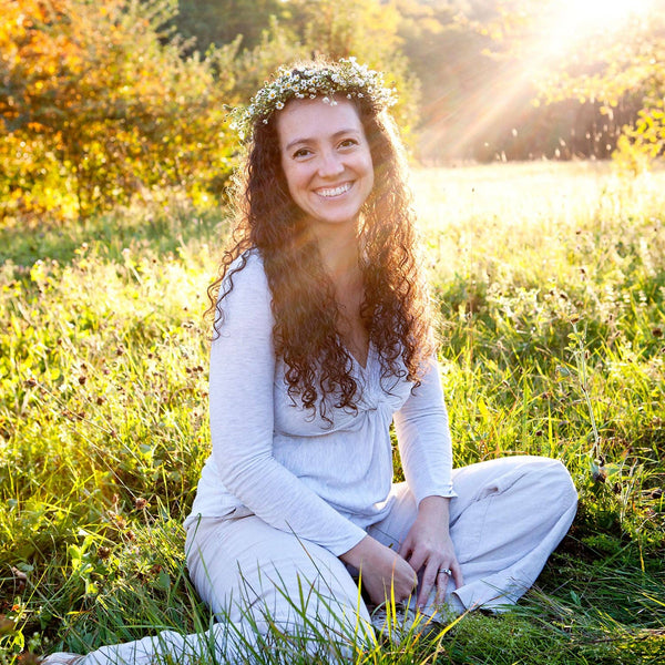 Potager Soap Co. Badger Rose Body Oil promoted by a smiling woman with a flower crown sitting in a sunlit meadow.
