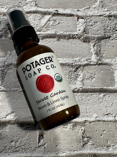 Potager Soap Co. Secret Garden organic room and linen spray in a 2 oz amber glass bottle on a white brick background.