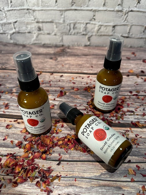 Three Potager Soap Co. Secret Garden organic room and linen spray bottles in amber glass on a rustic wooden surface.