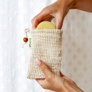 Potager Soap Co. sisal soap saver bag with drawstring and wooden bead, holding a round bar soap for exfoliation.