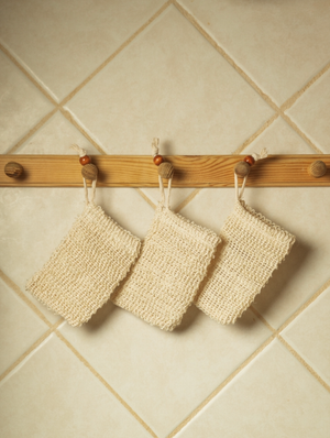 Three Potager Soap Co. natural sisal exfoliating soap saver bags hanging on a wooden rack against a tiled wall.