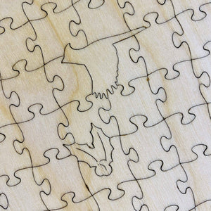 Potager Soap Co. wooden jigsaw puzzle pieces featuring a unique bird-shaped whimsy piece on a light wood grain surface.