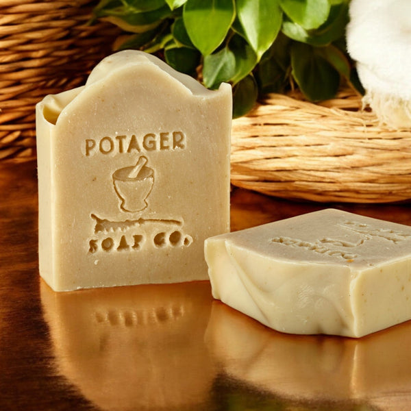 Two bars of soap with 'Potager Soap Co.' branding on a reflective surface.