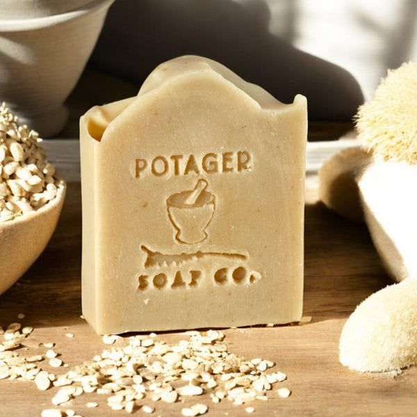 Bar of soap with 'Potager Soap Co.' branding on a wooden surface with organic oats and a pot.
